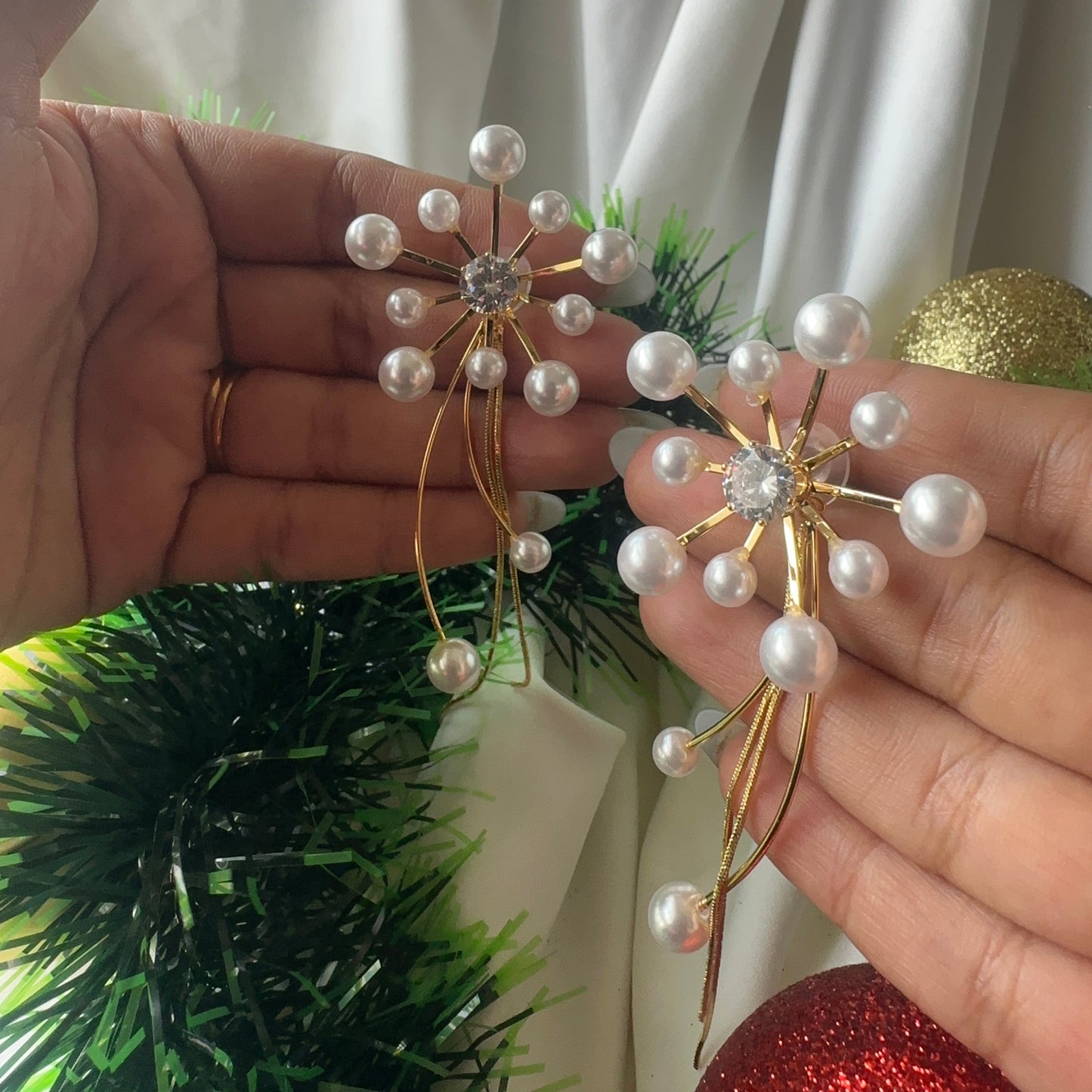 Hand holding a decorative item with pearls and gold elements against a neutral background